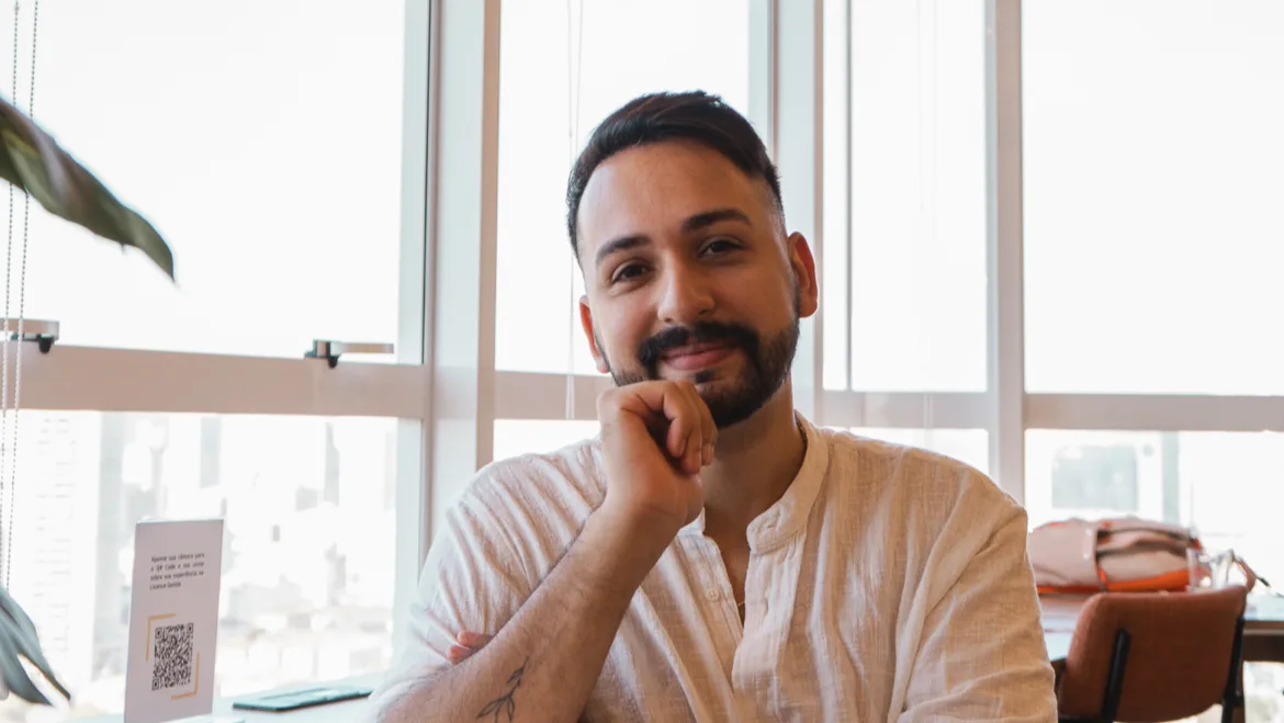 Victor Luz sorrindo, sentado perto de janelas claras